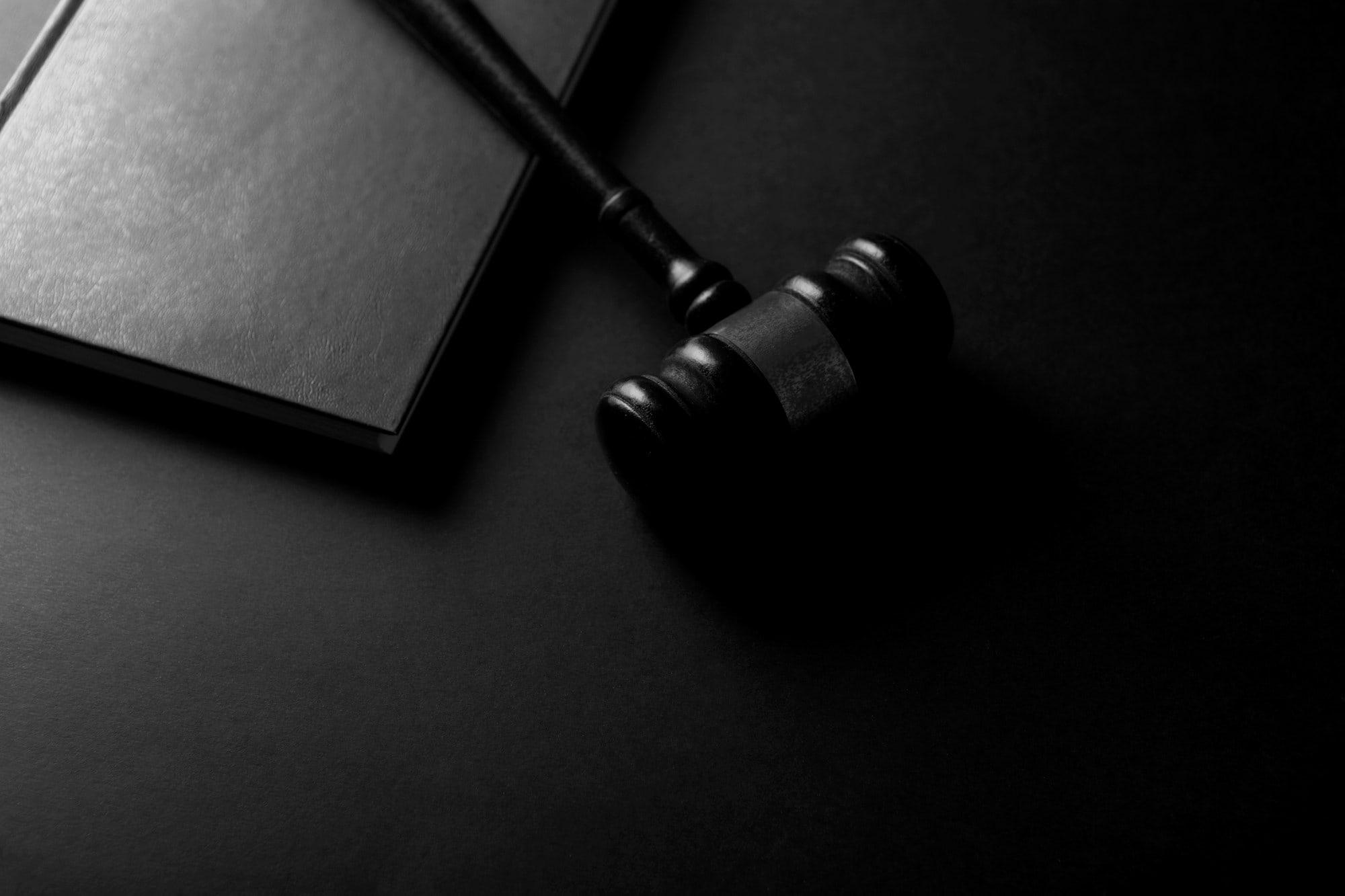 Scales, law books and a gavel on a dark desk, in black and white.