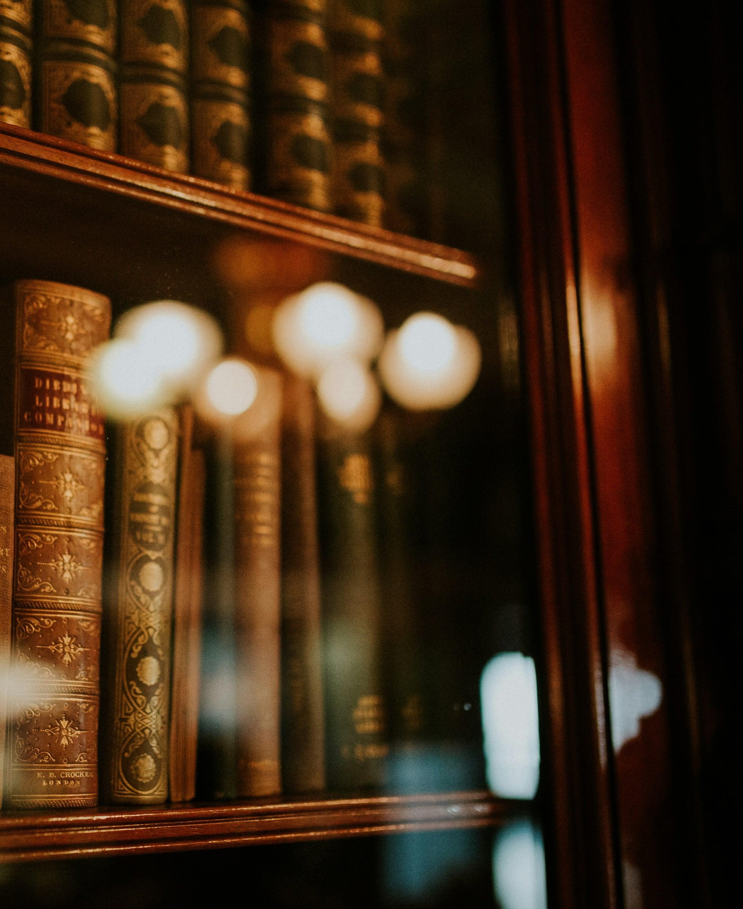 Antique leather-bound books behind the glass door of a mahogany bookcase, lit warmly.